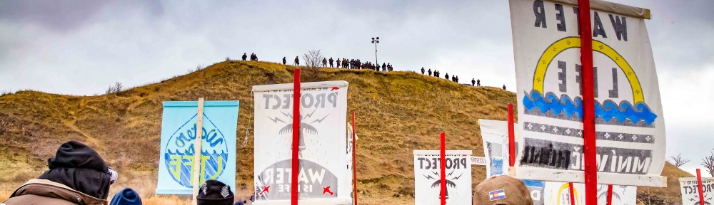 Water protectors hold signs facing armed police atop sacred burial site, Turtle Island, on November 24, 2016.